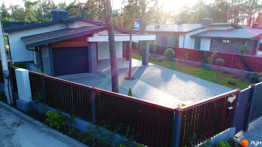 Зображення будинку в Котеджному містечку Хвойний квартал. На фото видно фасад будинку з гаражем, паркан та доглянуту прибудинкову територію з бруківкою.