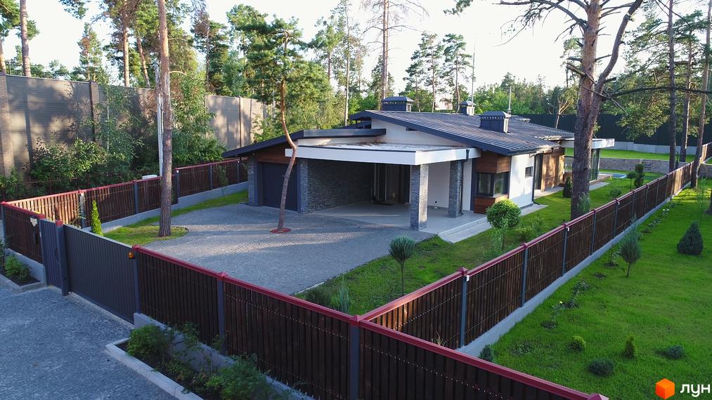 Зображення будинку в Котеджному містечку Хвойний квартал. На фото видно будинок з гаражем, парканом та доглянутою прибудинковою територією з газоном та деревами.