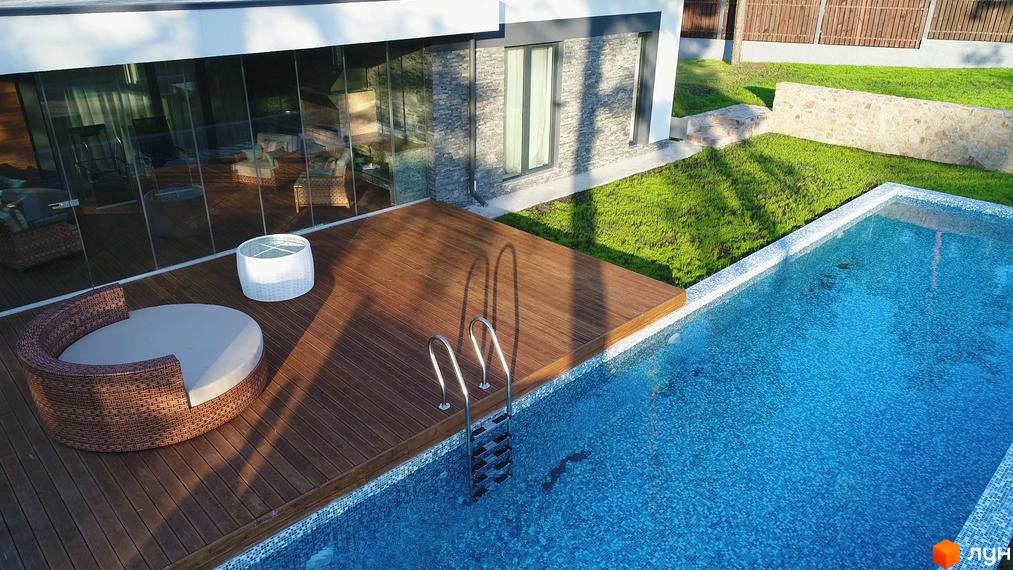 Будинок з панорамним склінням та дерев'яною терасою біля басейну. На території Котеджне містечко Хвойний квартал газон та зона відпочинку.