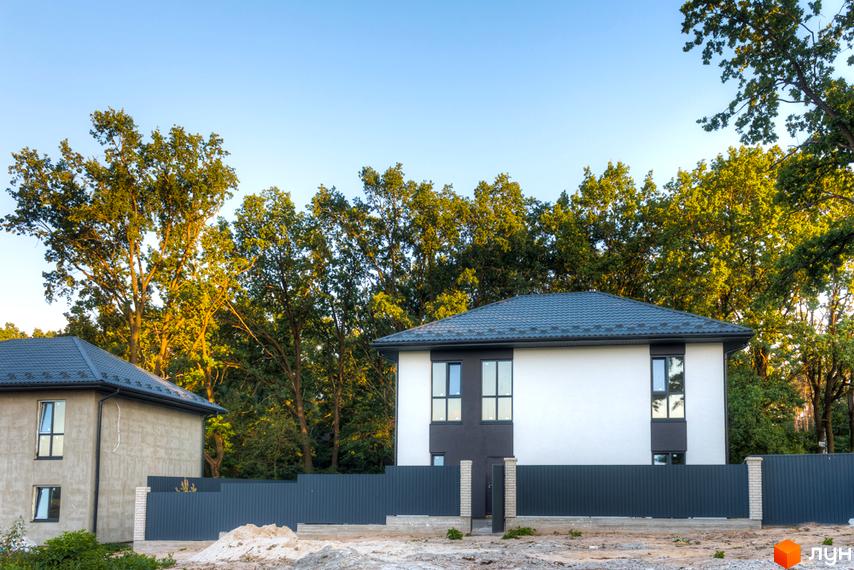 Зображення двоповерхового будинку в Котеджному містечку Lion`s Nest. Навколо будинку дерева та сірий паркан.