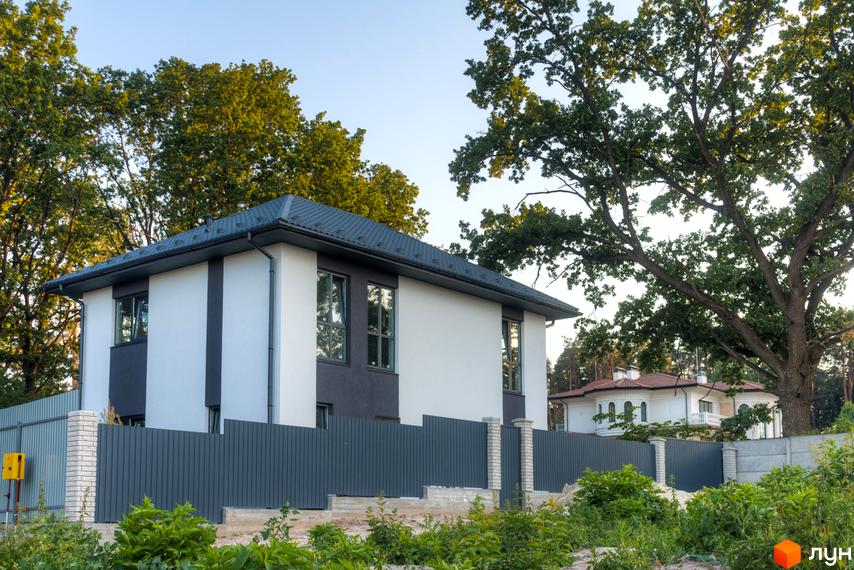 Зображення двоповерхового будинку в Котеджному містечку Lion`s Nest з сірим парканом та зеленими насадженнями. Вигляд екстер'єру будинку та прибудинкової території.