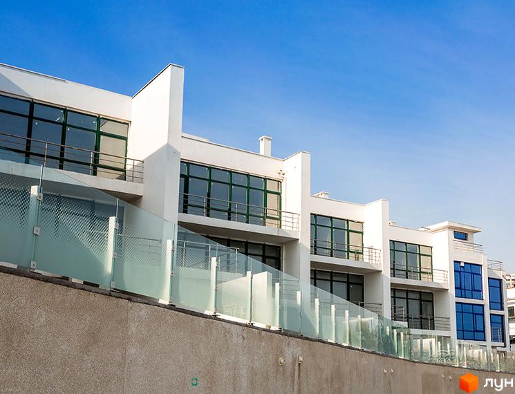 Зображення фасаду Котеджного містечка Santa Bay. Двоповерхові будинки з великими вікнами та скляними огорожами балконів на тлі блакитного неба.