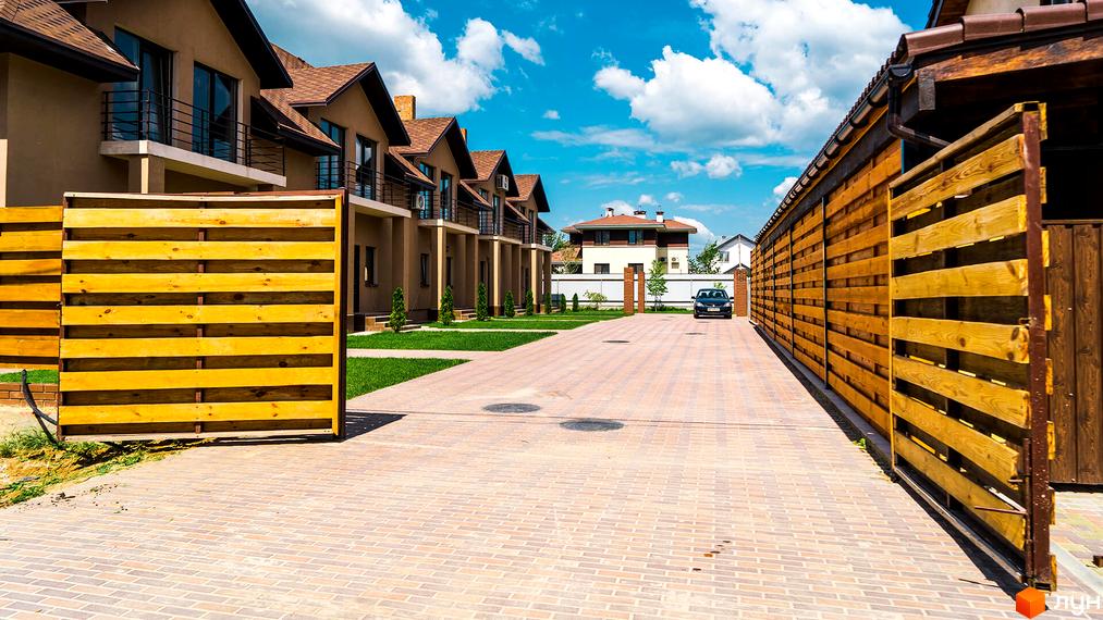 Житловий комплекс на Дорошенка, 7: будинки з коричневими дахами, балконами, вимощена дорога, зелені газони та дерев'яні паркани.