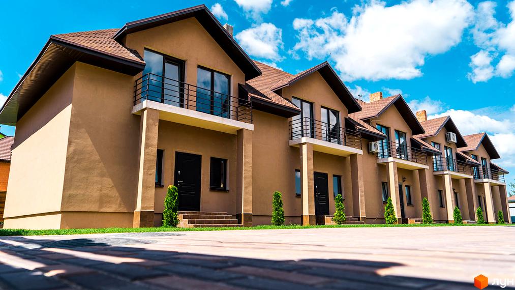 Зображення житлового комплексу по вулиці Дорошенка, 7. Світлі будинки з коричневими дахами та балконами на тлі блакитного неба.