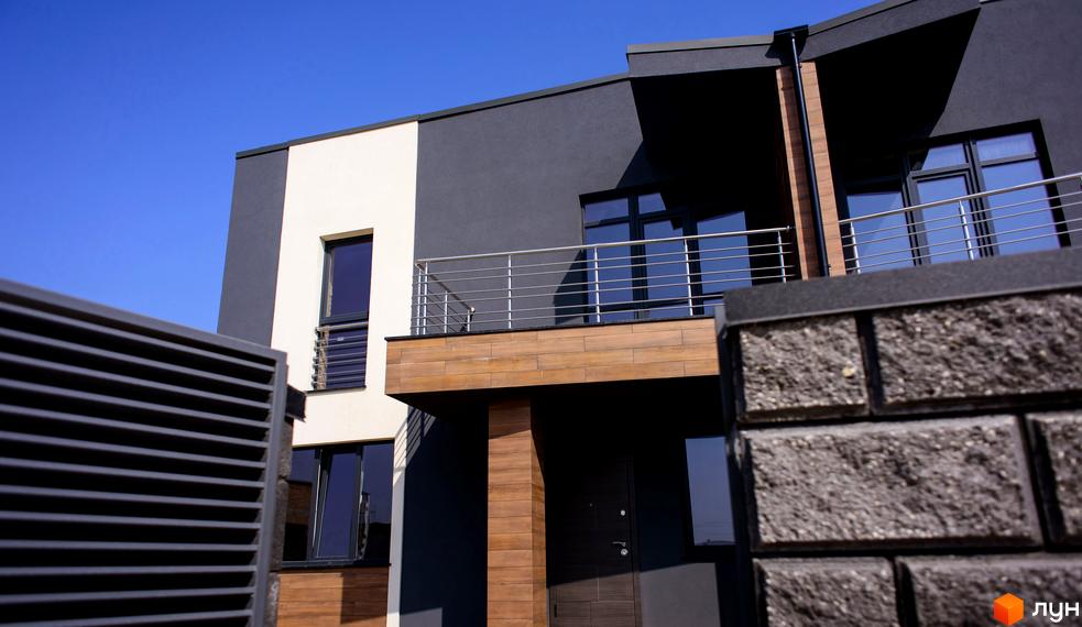 Зовнішній вигляд таунхаусу „Elegant“ з фасадом у сірих тонах та дерев'яними елементами. На передньому плані — огорожа з декоративного каменю.