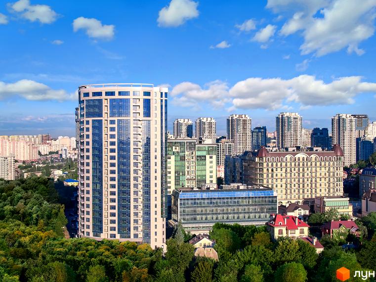 Житловий комплекс Busov Hill – висотна будівля з панорамними вікнами та сучасним фасадом на тлі блакитного неба. Навколо зелені дерева та інші будівлі міста.