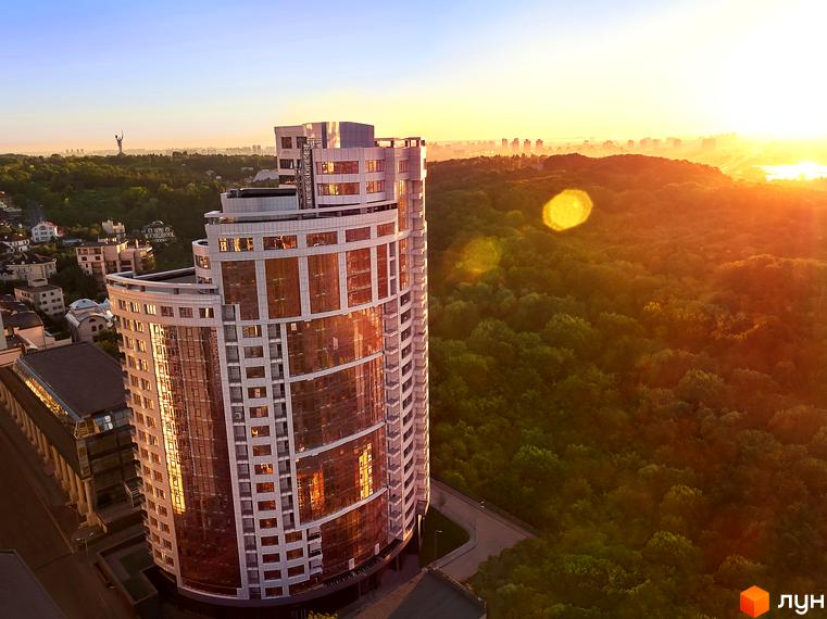 Житловий комплекс Busov Hill з панорамними вікнами на фоні сходу сонця. Навколо комплексу зелені дерева та міський пейзаж.