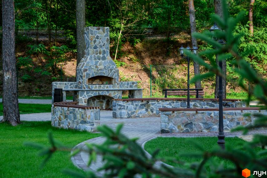 Житловий комплекс DESNA residence з цегляним барбекю комплексом та лавками на прибудинковій території. Зелена галявина та дерева навколо.