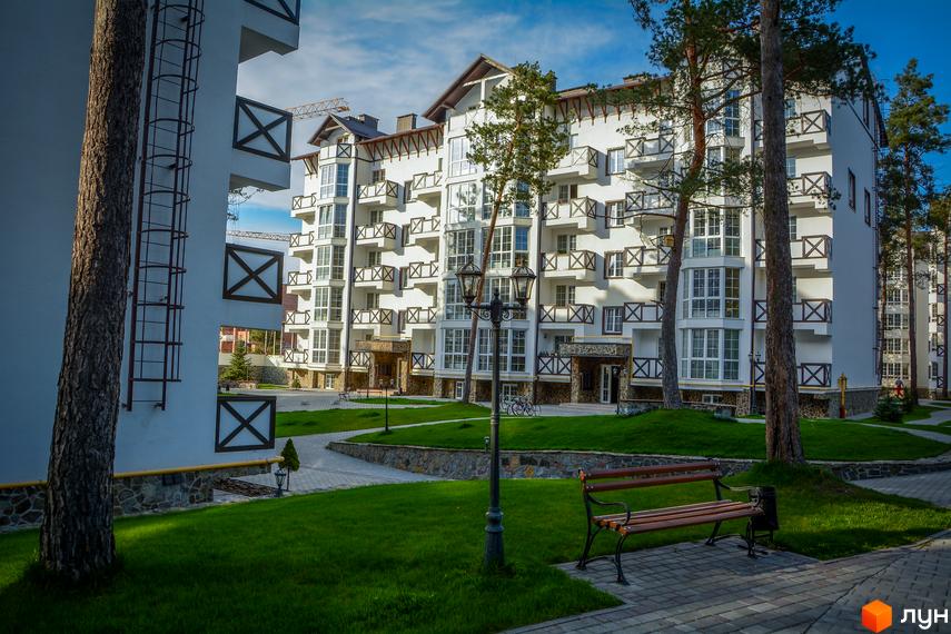 Зовнішній вигляд новобудови ЖК DESNA residence з балконами та вікнами. Прибудинкова територія з газоном, лавкою та ліхтарем.