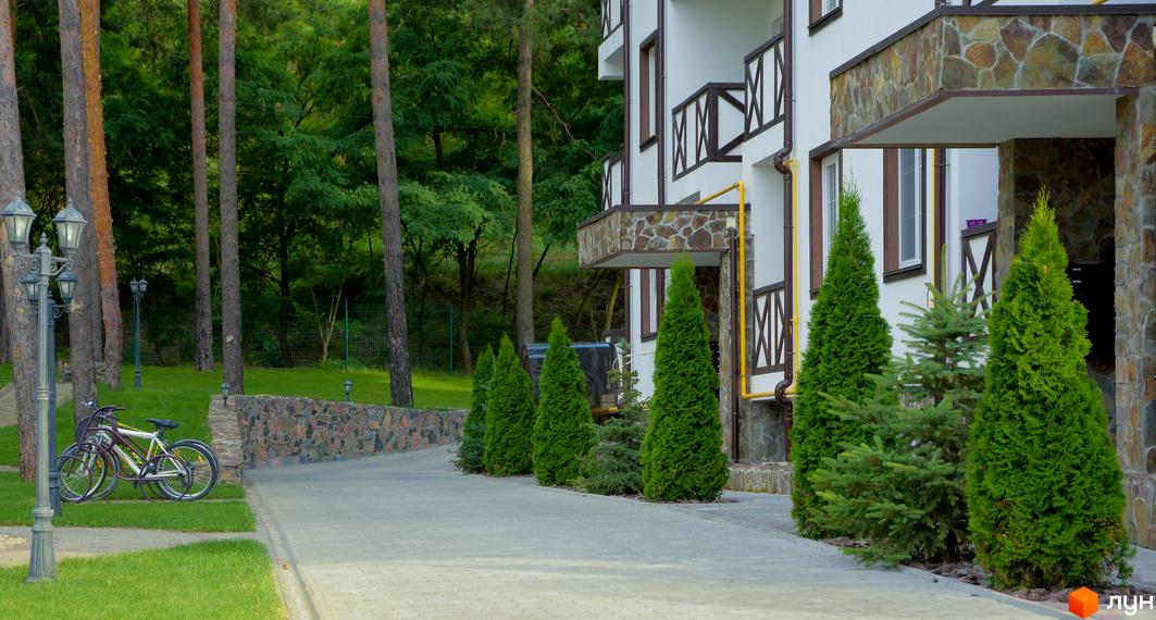 Житловий комплекс DESNA residence з фасадом з каменю та деревини. Прибудинкова територія з акуратними туями та велосипедами.