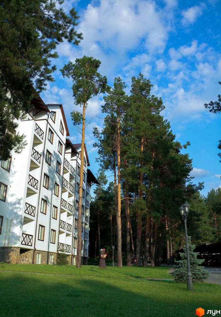 Житловий комплекс DESNA residence: біла будівля з дерев'яними балконами на тлі зеленої галявини та високих сосен.