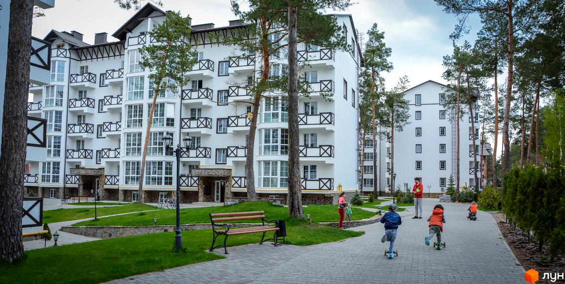 Житловий комплекс DESNA residence з білою фасадною обробкою та дерев'яними елементами. На прибудинковій території облаштований зелений двір з лавочками та доріжками.