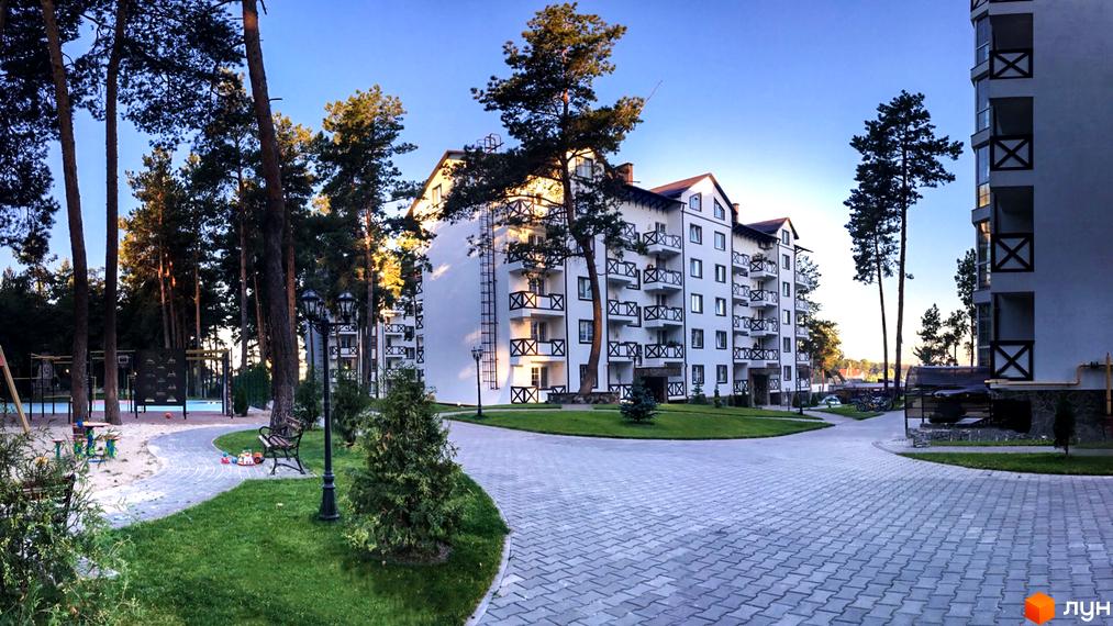 Житловий комплекс DESNA residence з білими фасадами та балконами, оточений соснами. На прибудинковій території облаштований дитячий майданчик та зони відпочинку.