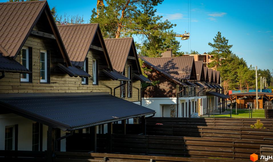 Таунхауси Desna Residence з коричневими дахами та дерев'яними фасадами. На території комплексу зелений газон та дерев'яна огорожа.