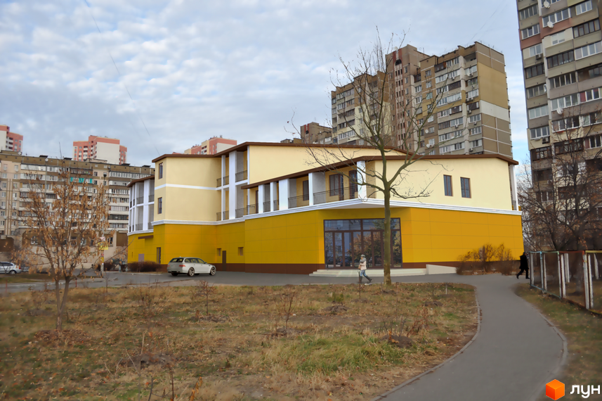 Житловий комплекс Милославський: жовта новобудова з білими елементами та балконами. Навколо будівлі розташована прибудинкова територія з деревами та доріжками.