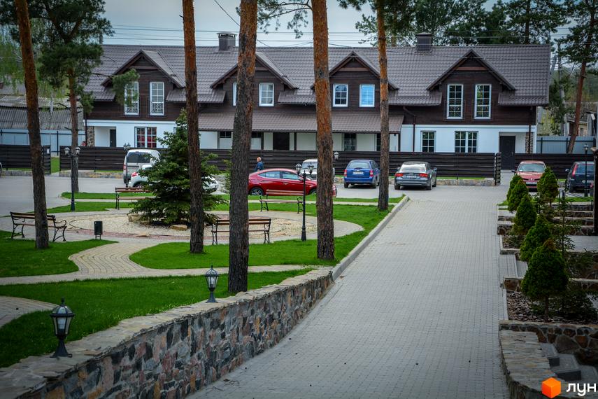 Таунхаус „Desna Residence“ з коричневим дахом та фасадом, оточений зеленим газоном та вимощеною доріжкою. На території є лавки та ліхтарі.