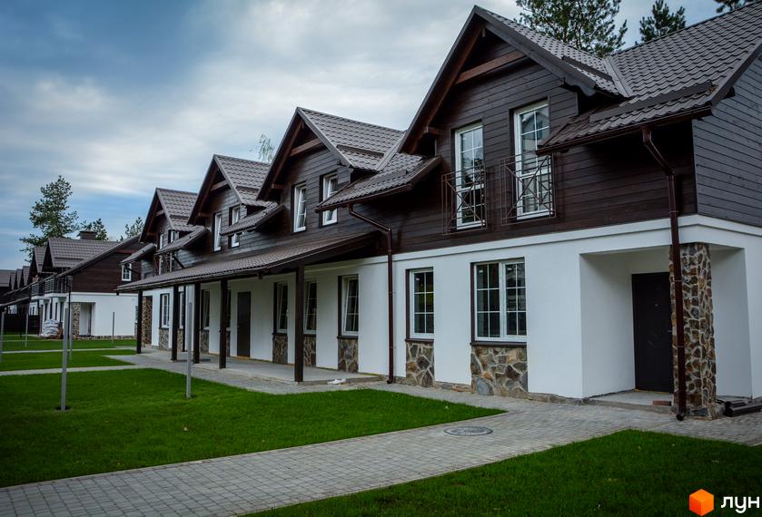 Таунхаус Desna Residence з коричневою дерев'яною обшивкою та білими стінами. Охайна прибудинкова територія з газоном та доріжками.