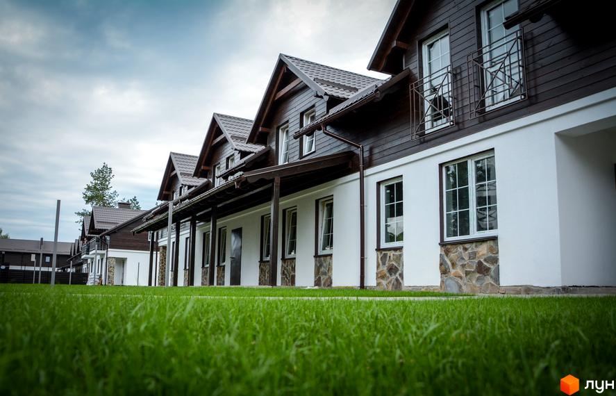 Таунхаус Desna Residence: двоповерхові будинки з коричневими дахами та дерев'яними фасадами, білими стінами та кам'яним оздобленням цоколя. Охайний зелений газон перед будинками.