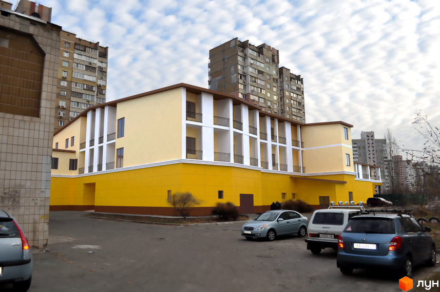 Зовнішній вигляд новобудови ЖК Милославський з жовтим фасадом та балконами. Прибудинкова територія з автомобілями.