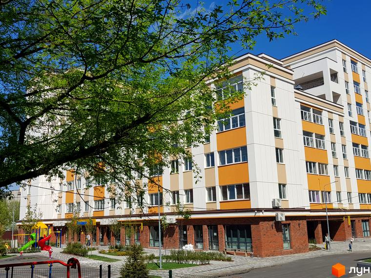 Клубний будинок Fort House з біло-жовтими фасадами та цегляним цоколем. Поруч дитячий майданчик та зелені насадження.