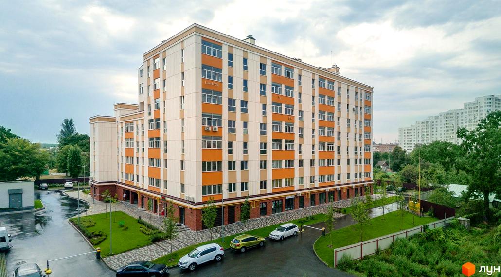 Зображення будинку в Клубному будинку Fort House. Багатоповерхова будівля з помаранчевими вставками, поруч зелена територія з деревами та парковкою.