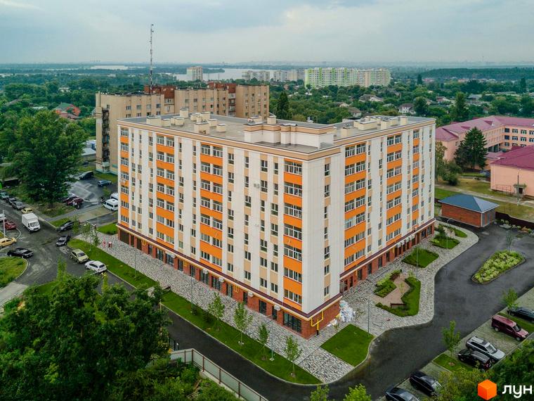 Клубний будинок Fort House з біло-помаранчевим фасадом та численними вікнами. Навколо будинку облаштована прибудинкова територія з парковкою та зеленими зонами.