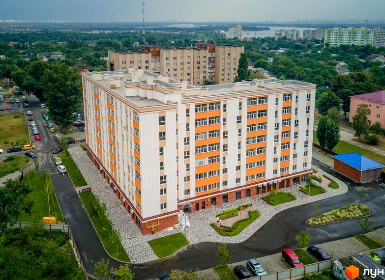 Клубний будинок Fort House з біло-помаранчевим фасадом та численними вікнами. Прибудинкова територія з доглянутими зеленими зонами, доріжками та місцями для паркування.