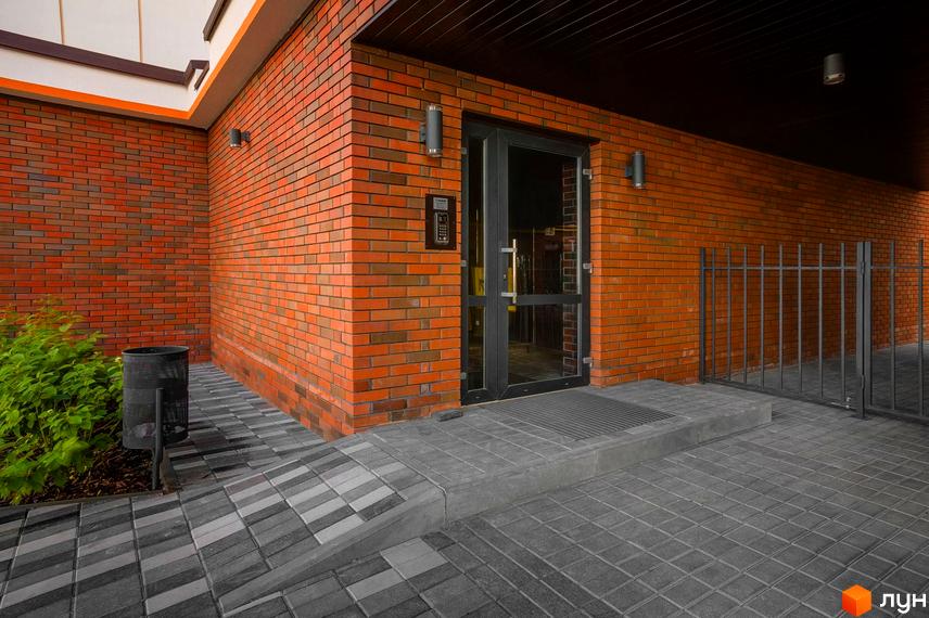 Клубний будинок Fort House з цегляним фасадом та скляними дверима. Прибудинкова територія з бруківкою та огорожею.