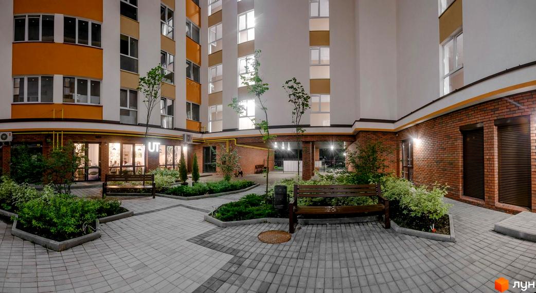 Зображення фасаду та внутрішнього двору Клубного будинку Fort House. Вигляд на будівлю з лавками, деревами та тротуарною плиткою.