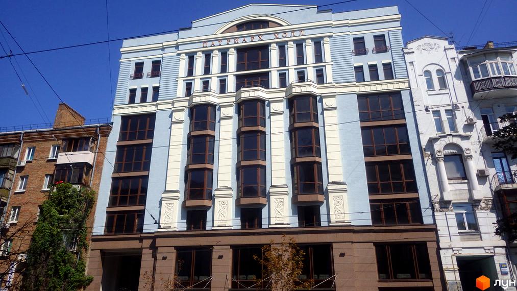 Клубний будинок „Патріарх Холл“ з великими вікнами та світлим фасадом. Будинок розташований на вулиці з іншими будівлями.