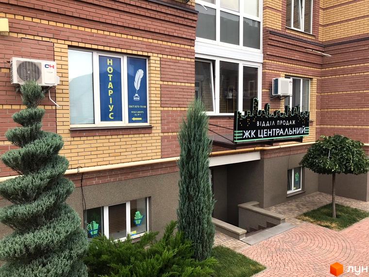 Зовнішній вигляд будинку ЖК Центральний з фасадом з цегли. Поряд з будівлею розташовані зелені насадження та доглянута прибудинкова територія.