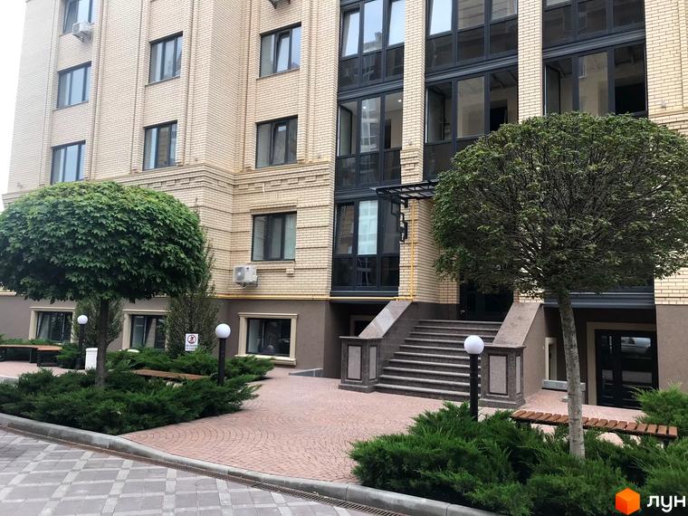 Зовнішній вигляд будівлі Житловий комплекс Центральний з цегляними фасадами та великими вікнами. На прибудинковій території розташовані зелені насадження, лавки та ліхтарі.