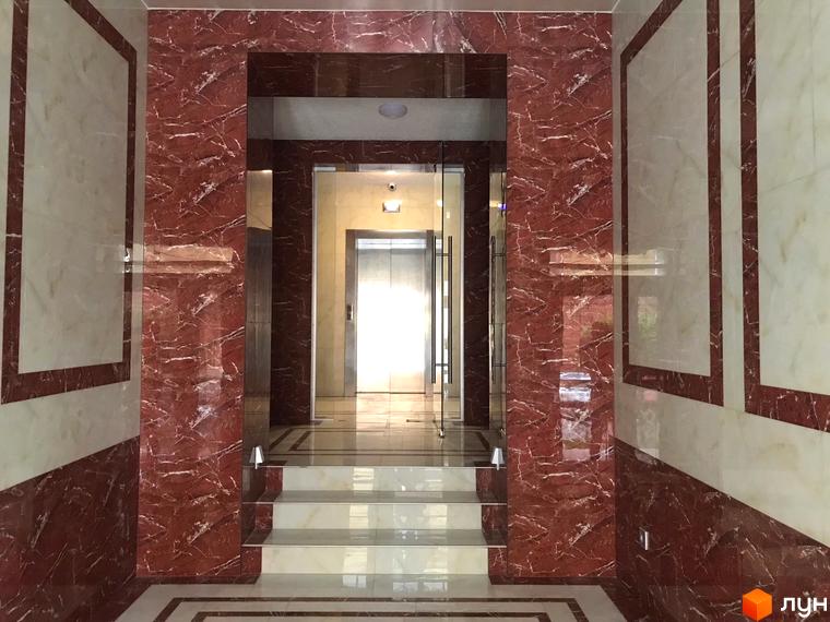 Інтер'єр ЖК Центральний. Просторий хол з мармуровим оздобленням стін та підлоги. Сходи ведуть до ліфтів, створюючи атмосферу розкоші та комфорту.