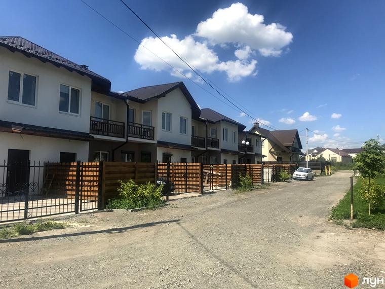 Котеджне містечко Riviera. Двоповерхові будинки з балконами та коричневими дахами. Перед будинками розташована огорожа з дерева та металу, а також невелика прибудинкова територія.