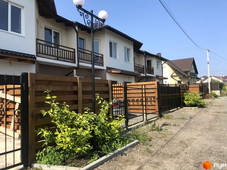 Котеджне містечко Riviera: двоповерхові будинки світлих тонів з балконами. Територія облаштована дерев'яним парканом та зеленими насадженнями.