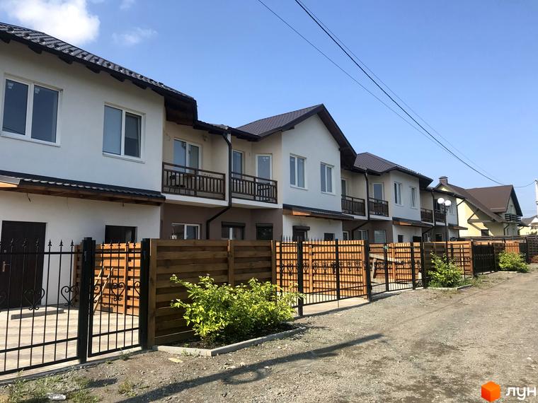 Котеджний комплекс Riviera: ряд двоповерхових будинків з балконами, світлими фасадами та темними дахами. Прибудинкова територія має ґрунтову дорогу та комбіновані огорожі.