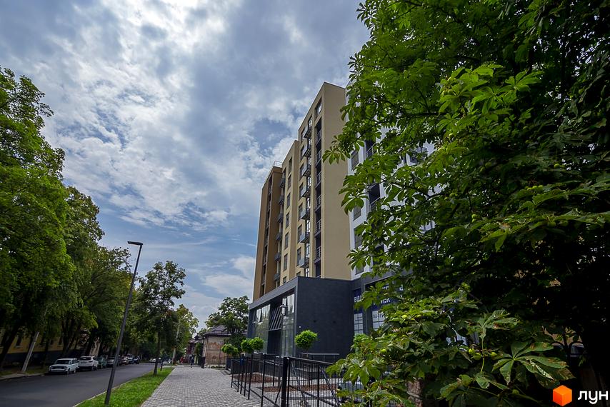 Житловий комплекс White Tower - висотна будівля з балконами та вікнами. Поруч розташована доглянута прибудинкова територія з пішохідною доріжкою та деревами.