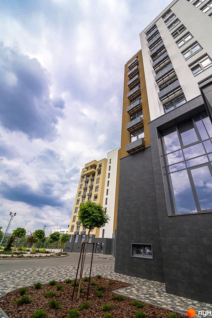 Житловий комплекс White Tower з білим фасадом та балконами. Навколо облаштована прибудинкова територія з доріжками та деревами.