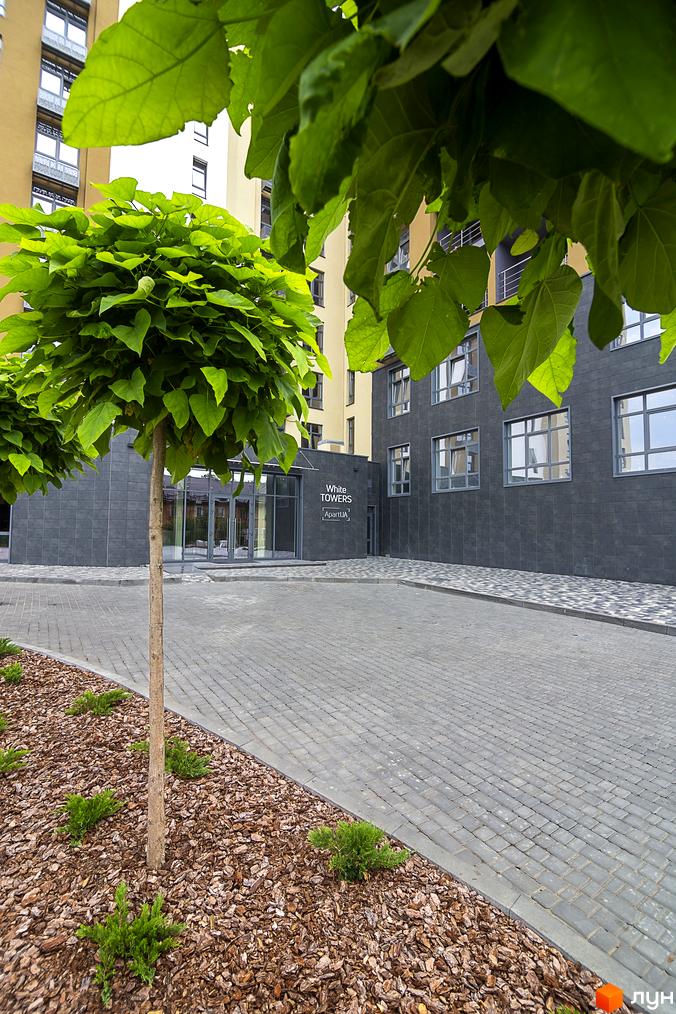 Зовнішній вигляд новобудови White Towers ApartUA з комбінованими фасадами та численними вікнами. Прибудинкова територія має бруковані доріжки та зелені насадження.