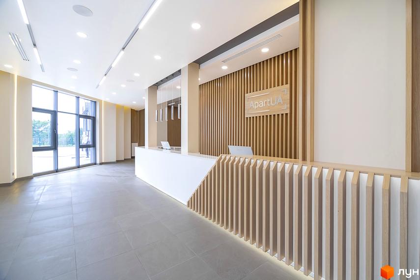 Стійка реєстрації в новобудові White Tower з дерев'яними елементами та логотипом компанії. Просторий хол з великими вікнами та сірою плиткою на підлозі.