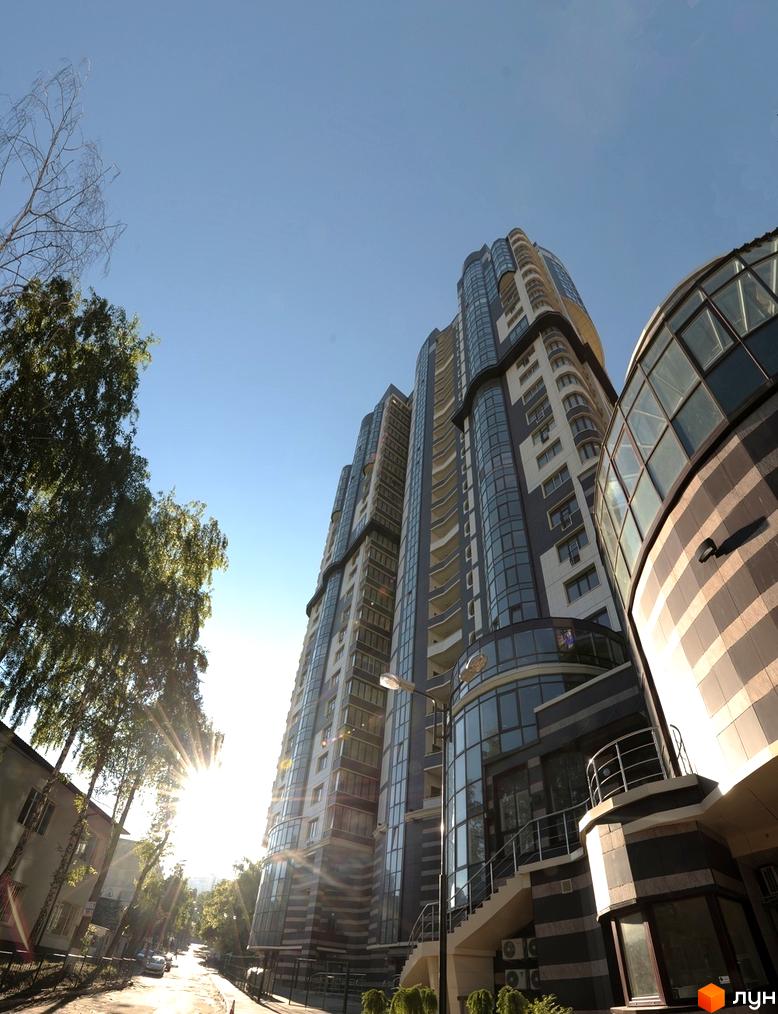 Багатоповерховий будинок Житловий комплекс Престиж Холл з вигнутими фасадами та великими вікнами. Навколо зелені дерева та дорога.