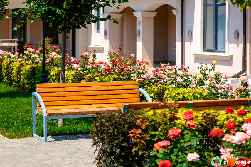 Житловий комплекс Таунхауси „Вілла Троянд“ з квітучими кущами та лавкою на прибудинковій території.