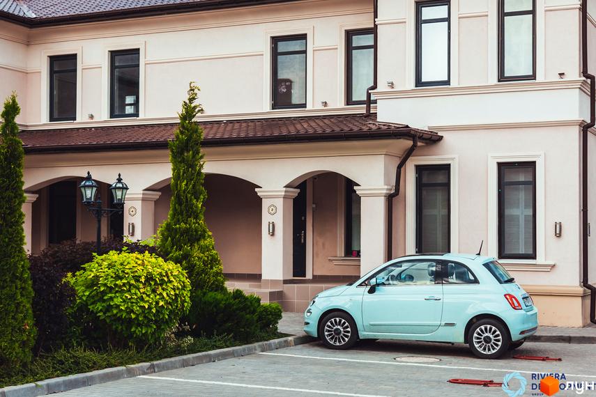 Зображення таунхаусів «Вілла Троянд» з автомобілем на парковці. Фасад будинку з вікнами та вхідною групою, зелені насадження.