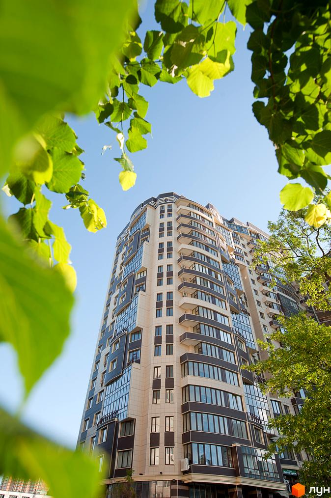 Житловий комплекс Престиж Холл: багатоповерховий будинок зі світлим та темним фасадом, великими вікнами та балконами, оточений зеленими деревами.