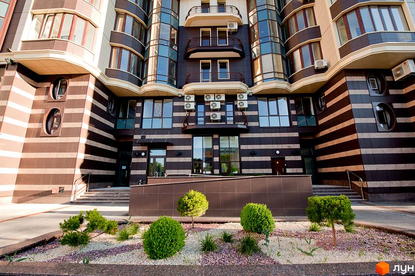 Житловий комплекс Престиж Холл: фасад з коричневими та світлими смугами, вікнами та балконами. Прибудинкова територія з кущами та гравієм.