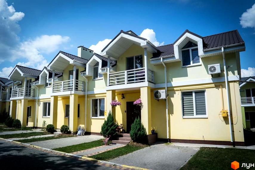 Зображення Котеджного містечка Sun City: двоповерхові будинки з балконами, жовті стіни та темні дахи. Перед будинками зелені газони та тротуарна плитка.