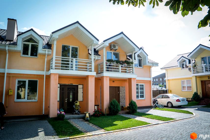 Зображення Котеджного містечка Sun City: двоповерхові будинки з балконами, акуратний двір з бруківкою та газонами. Світлі фасади та темні дахи.