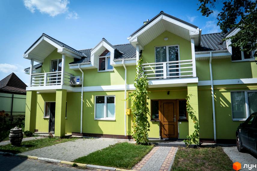 Зовнішній вигляд Котеджного містечка Sun City: двоповерхові котеджі з балконами та зеленим фасадом. Перед будинками газон та доріжки з тротуарної плитки.