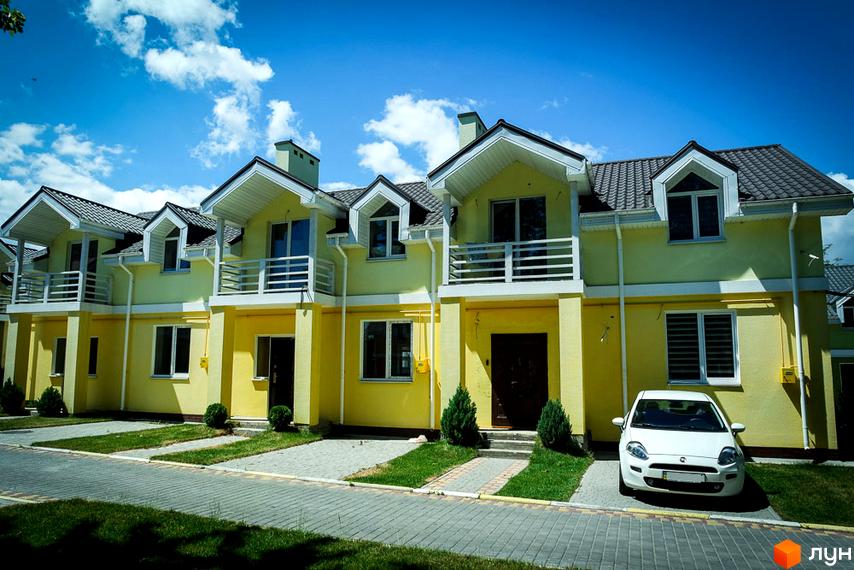 Зображення Котеджного містечка Sun City: жовті котеджі з мансардами та балконами, перед будинками зелені газони та припаркований білий автомобіль.