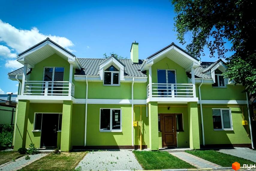 Зображення двоповерхового будинку Котеджного містечка Sun City з зеленим фасадом та сірим дахом. Перед будинком вимощена тротуарна плитка.